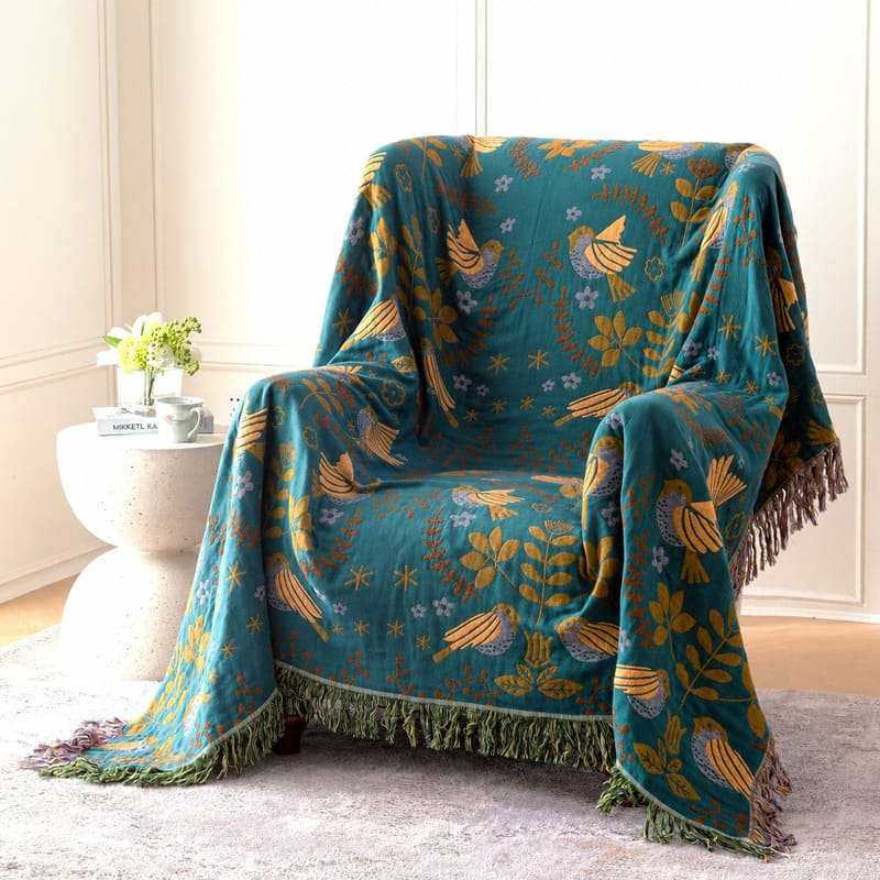 Reversible cotton throw blanket with bird and floral pattern draped over armchair in Nordic living room