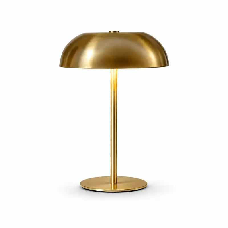 A modern table lamp with a brushed brass dome shade, a slim central stem, and a round base, shown on a clean white background.