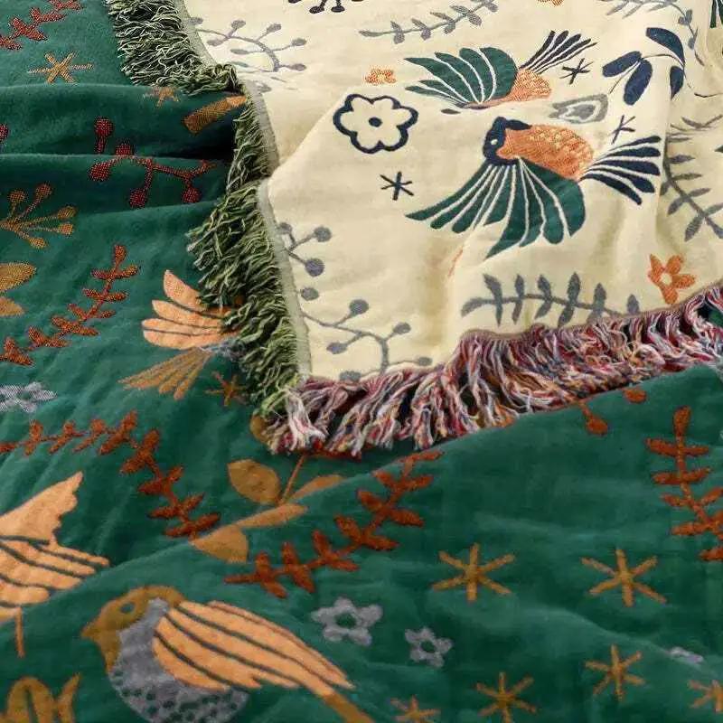 100% Cotton Reversible Throw Blanket draped over green and cream bird-pattern throws with fringe; decorative for sofa or bed.