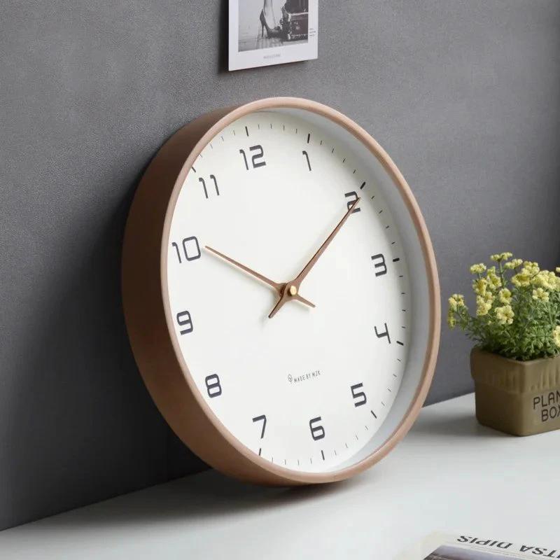 Nordic Wooden Wall Clock with white dial and copper hands, shown on a desk against a grey wall in a minimalist room.